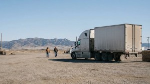 two workers walking near parked semi-truck trailer at rural gravel lot